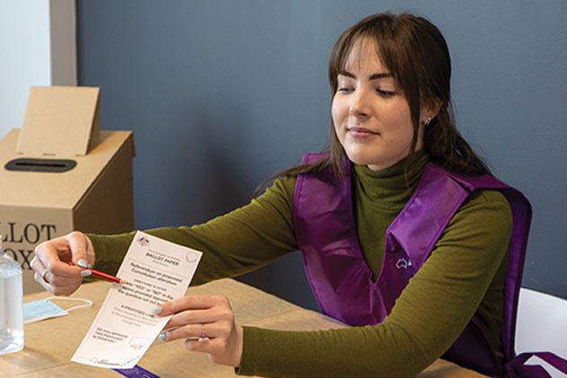 Woman in a purple AEC vest showing a voter how to fill in a referendum ballot paper