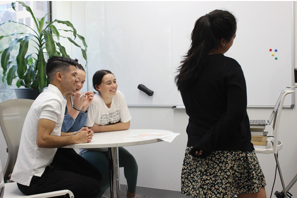 Group of young people sitting at table, looking happy and engaged in discussion