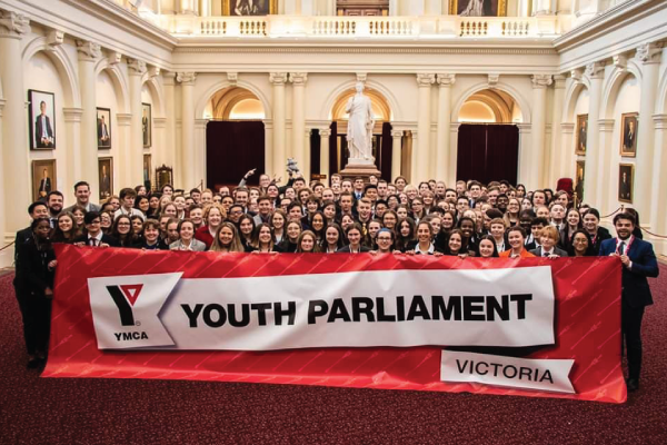 A large group of young people standing behind a banner that reads 'YMCA Youth Parliament'.