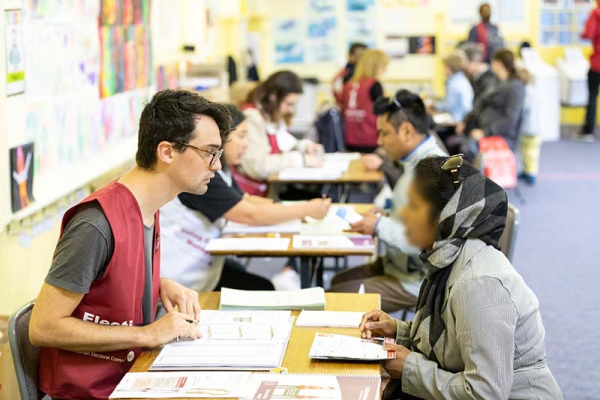 A row of people sitting at tables at a voting centre