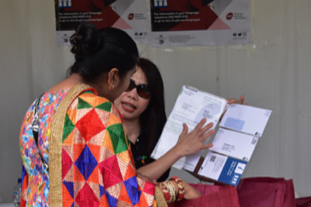 A VEC staff member explaining election materials to a community member at an outdoor event.