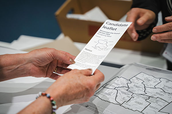 A pair of hands holding a leaflet with information about candidates.
